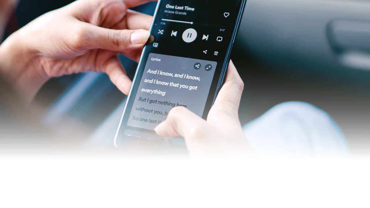 A person holds a smartphone displaying synced song lyrics on Spotify.