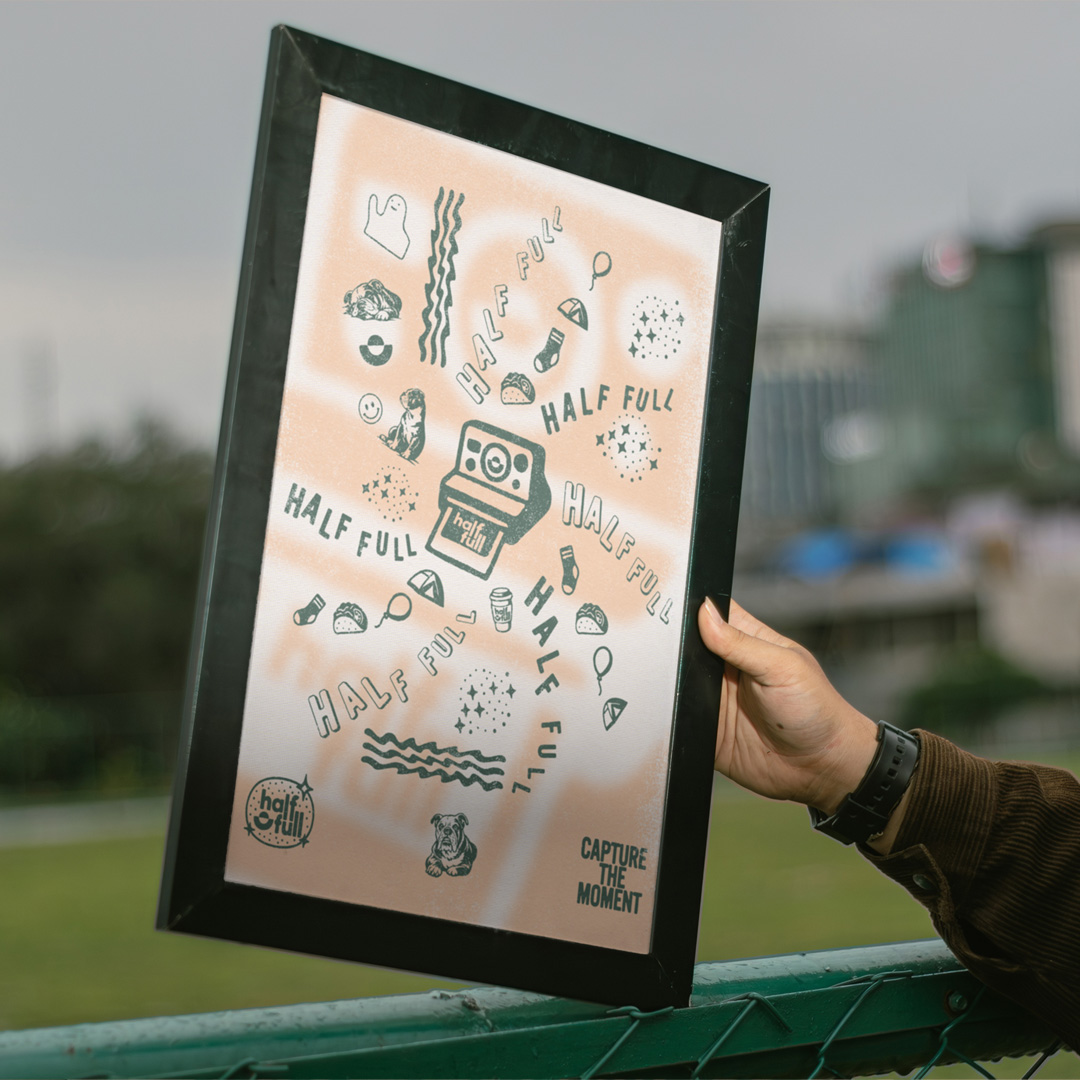 Hand holding a framed half full poster of green line illustrations around a camera, with the line Capture the Moment.