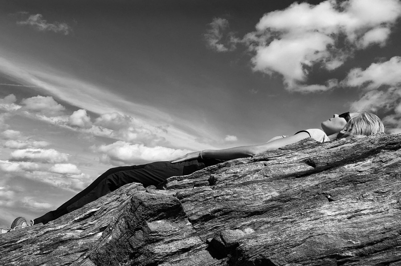 Donna distesa su roccia con nuvole, in un paesaggio in bianco e nero