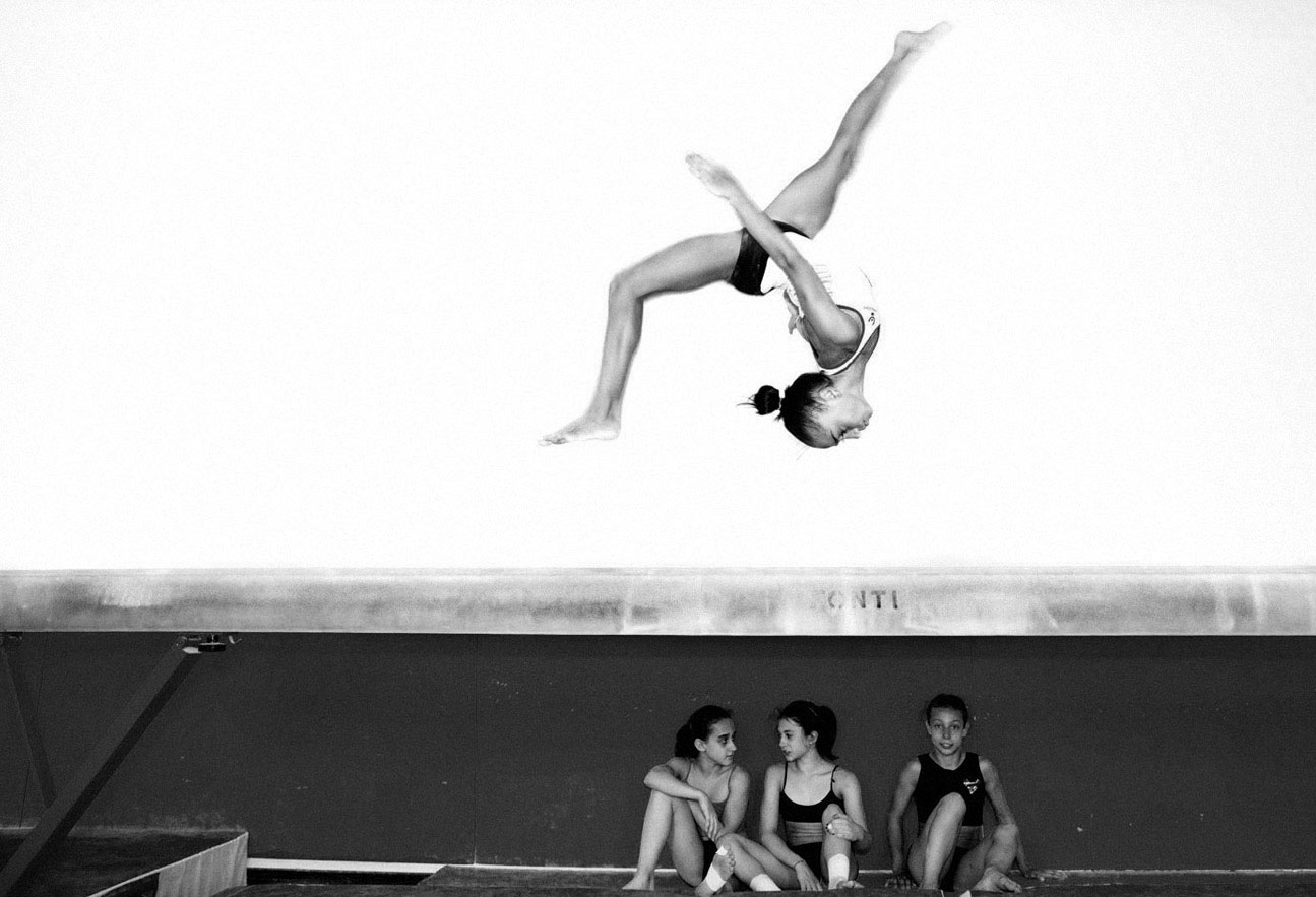Ginnasta in volo sopra compagne sedute durante allenamento