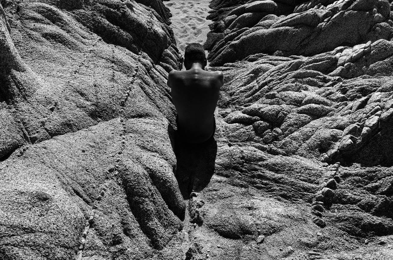 Figura solitaria tra le rocce contorte in un paesaggio sabbioso e aspro