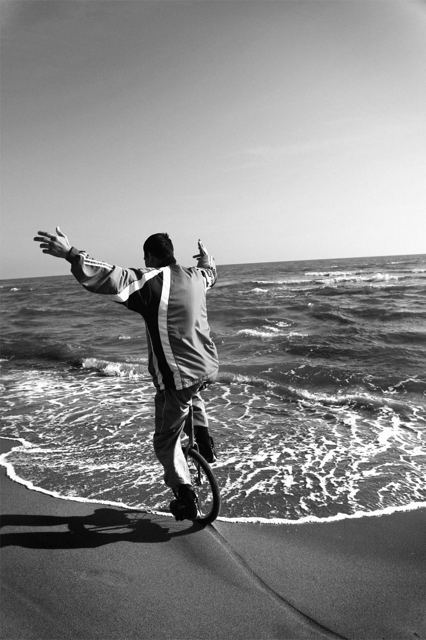 Persona in monociclo sulla spiaggia con onde e ombre, vista posteriore