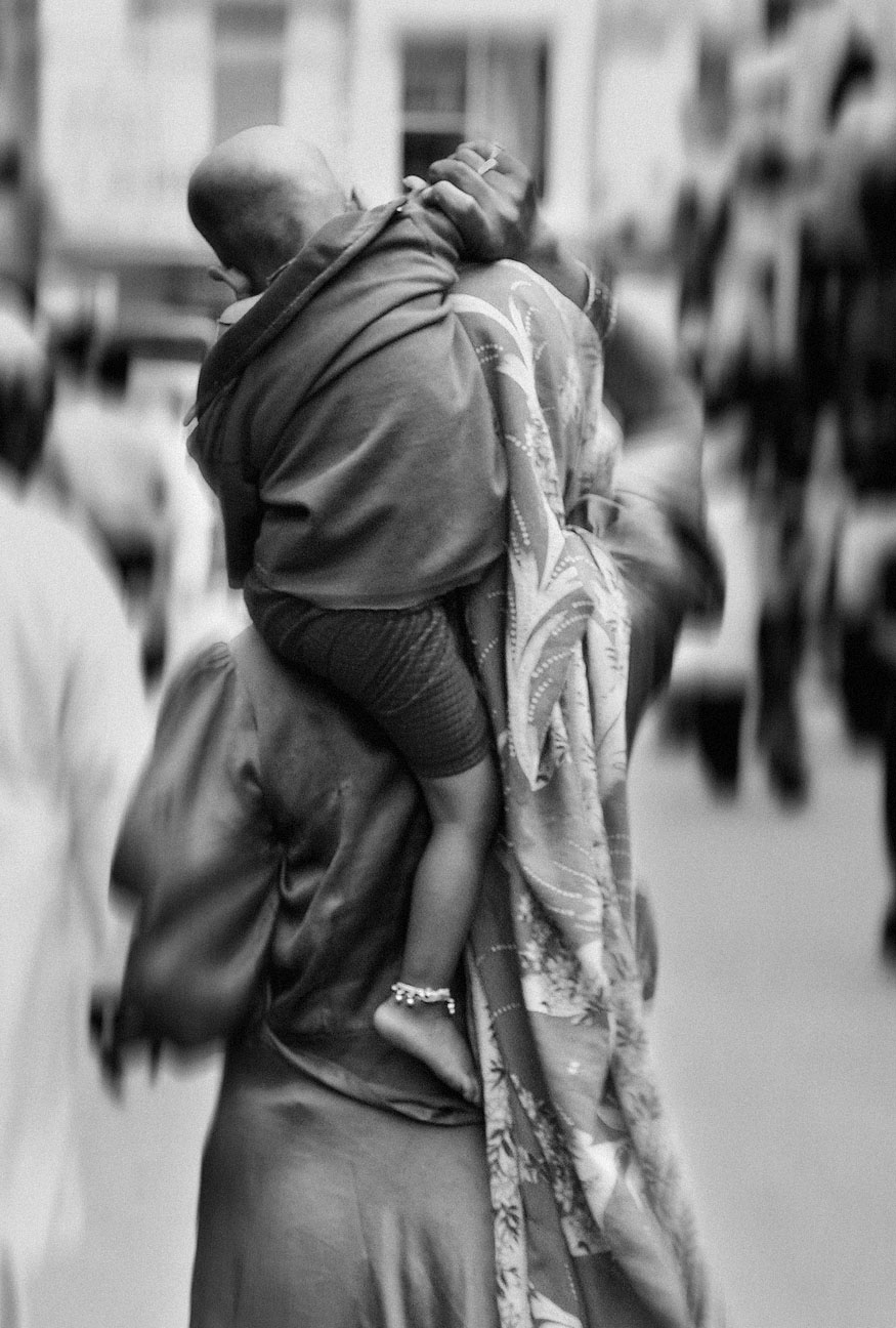 Donna con bambino in braccio, vestita in abiti tradizionali, vista posteriore