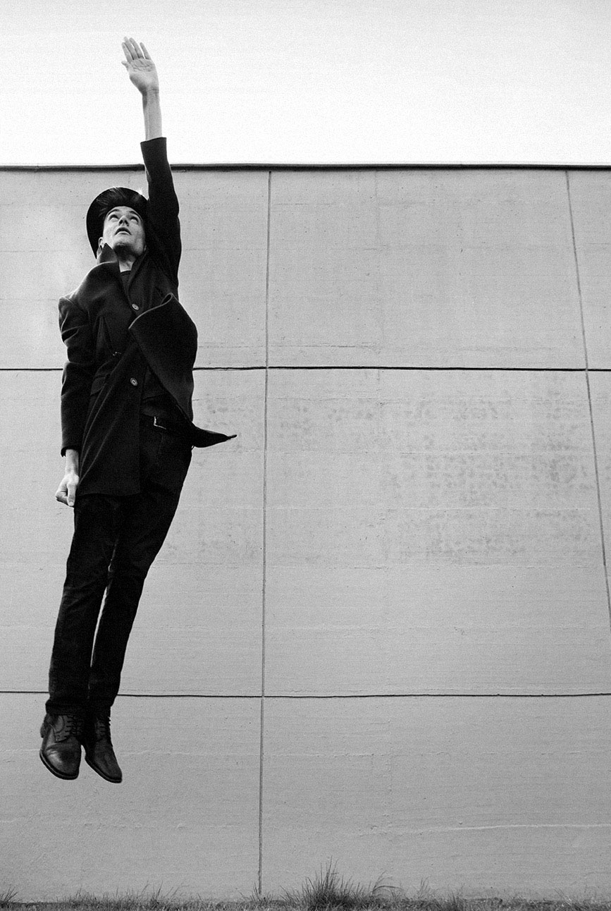 Persona in nero che salta verticalmente contro un muro grigio