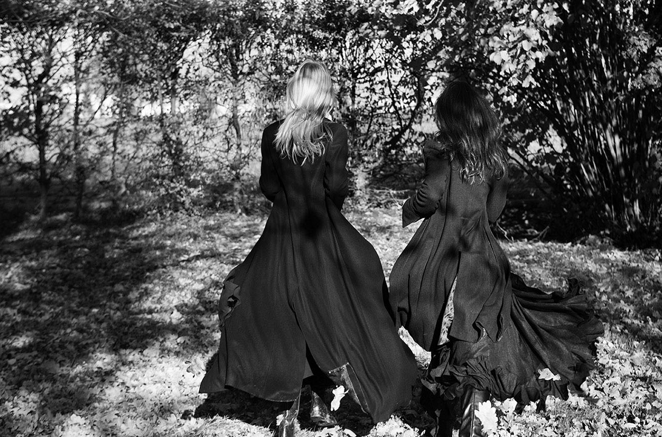 Due figure femminili in abiti neri camminano nel bosco in bianco e nero