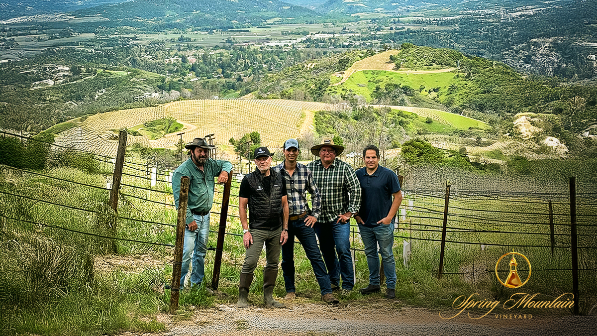 Vineyard team members pose together on a hillside overlooking the Napa Valley, with replanted vineyard blocks and scenic mountain views in the background.