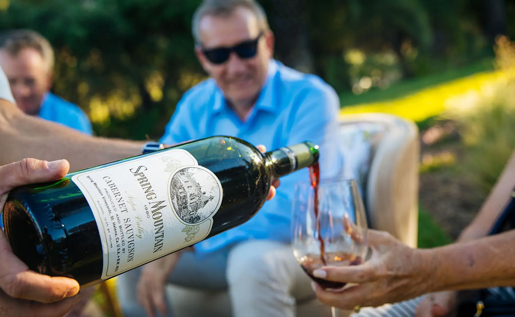 A couple on a swing facing the Napa Valley landscape at Spring Mountain Vineyard, with lush greenery, hills, and a clear blue sky.