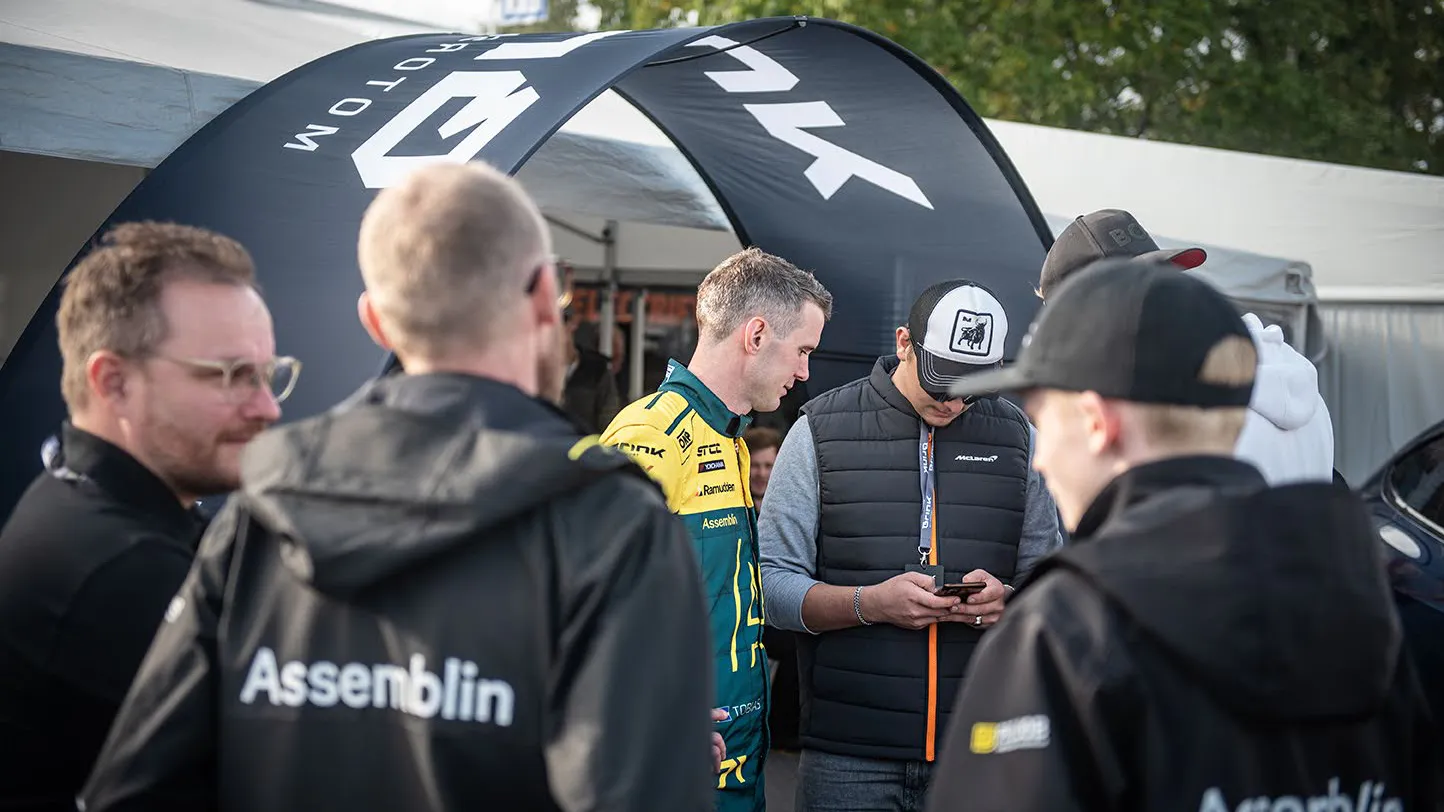 En grupp med män står runt ett tält och pratar. Någon tittar ner i telefonen.