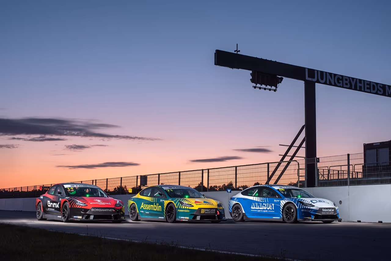 Tre bilar efter varandra vid startlinjen på en racingbana i solnedgången. 