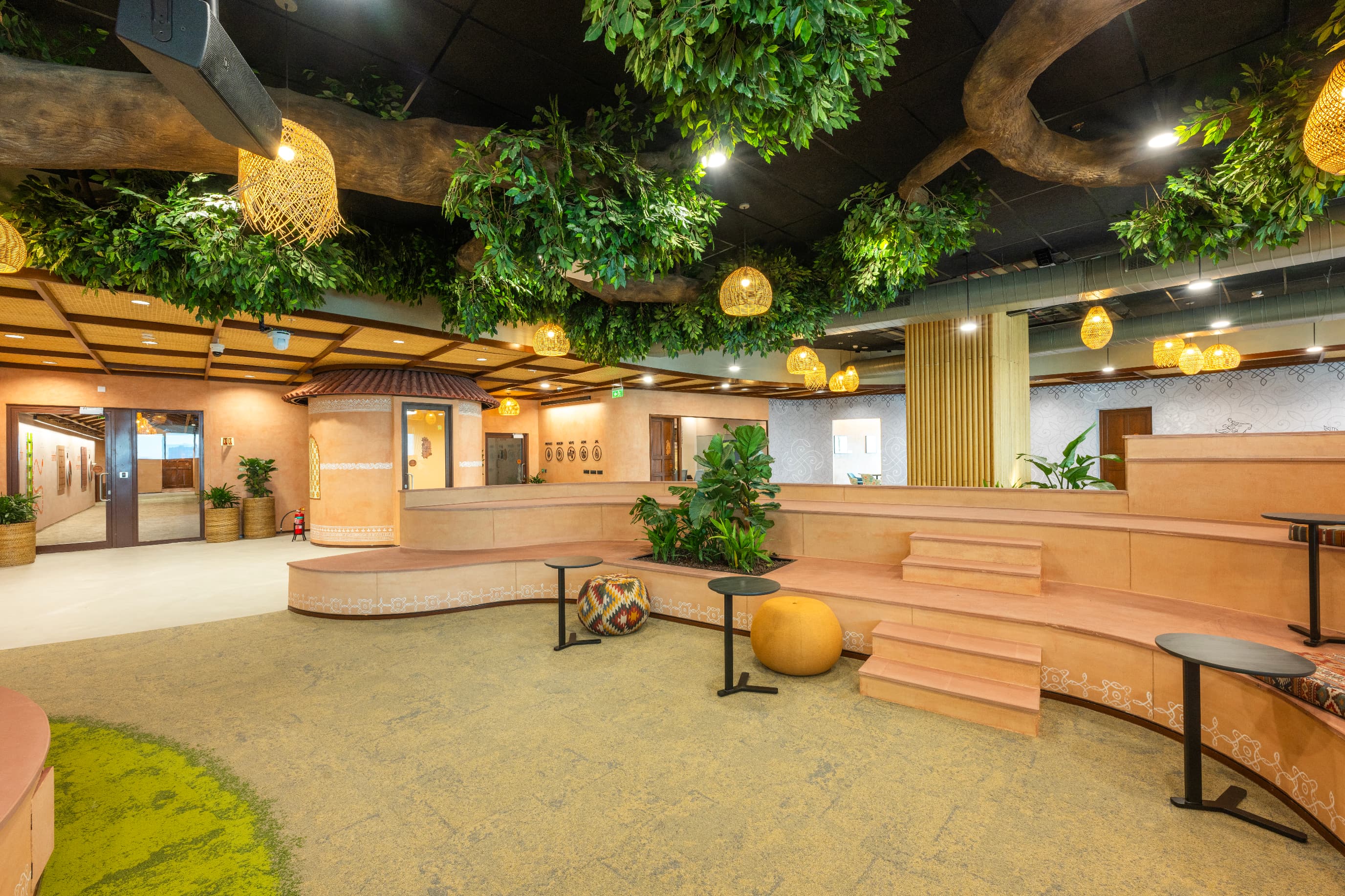 Earth-toned GRC walls carry the texture of rammed earth without the weight of solid clay. Focus huts crowned with Mangalore tile roofs occupy nooks and corners throughout the floor.