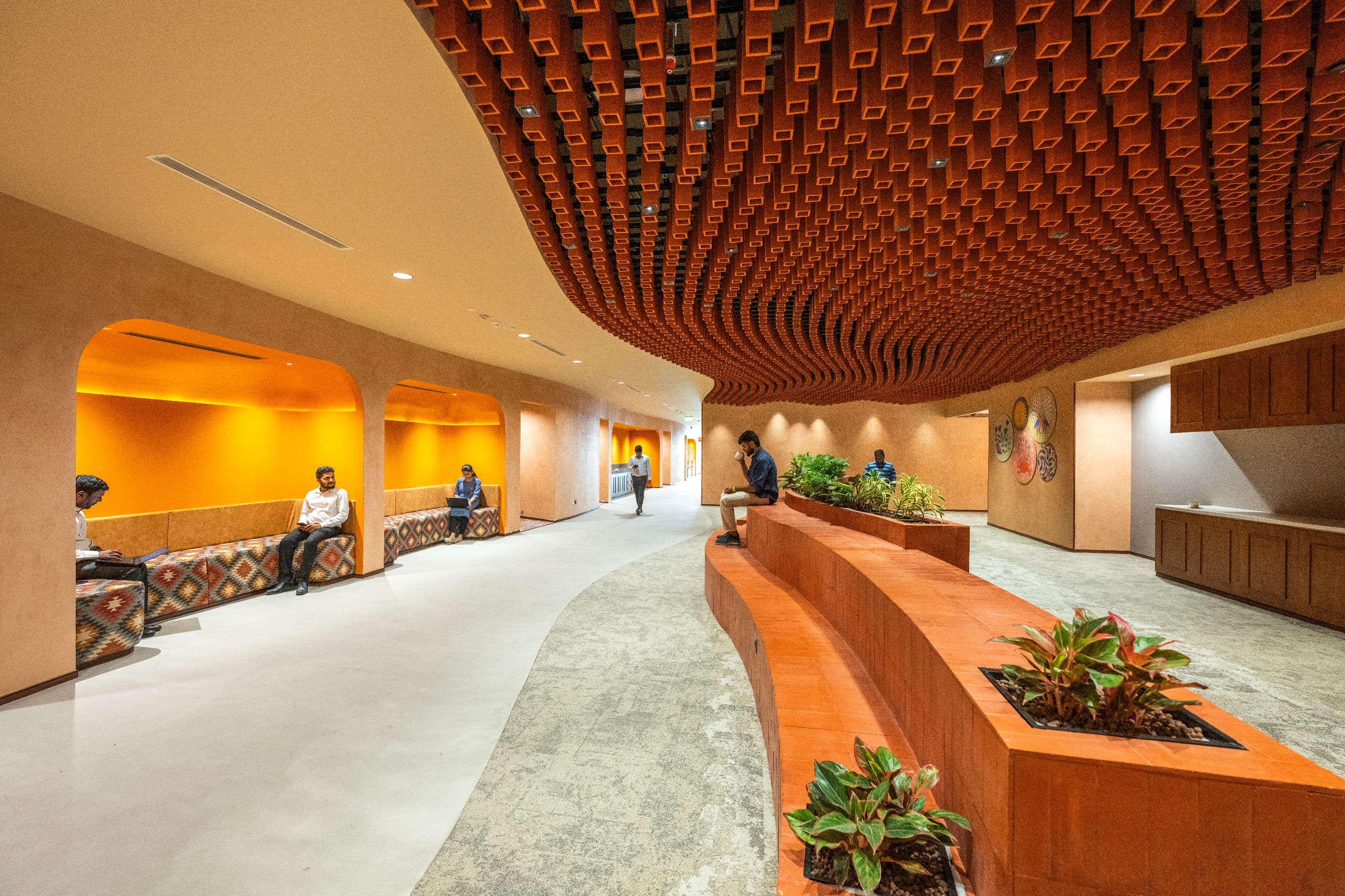 The main aisle runs beneath a parametrically modelled terracotta arcade with a soffit that ripples like a potter's wheel. Arched alcoves along it are upholstered in Indian-origin ikat and kalamkari.
