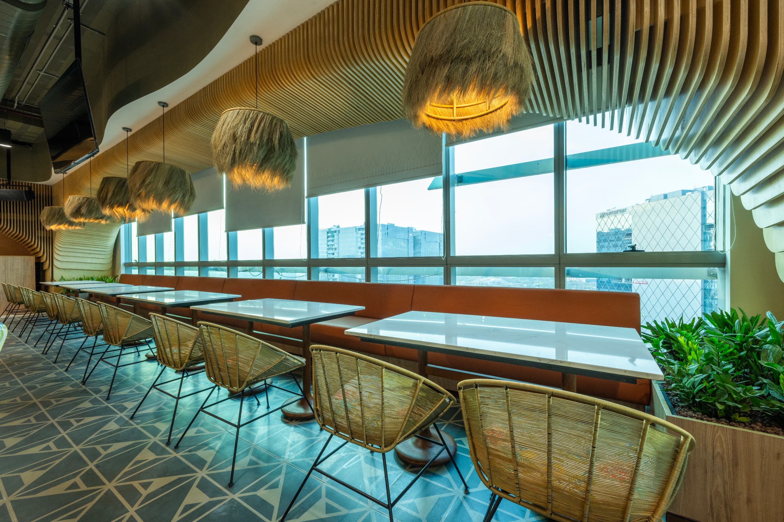 Window-side seating on the 20th floor looks out over HITEC City. Thatch pendants and a fluted timber soffit soften the edge between hospitality and workplace.
