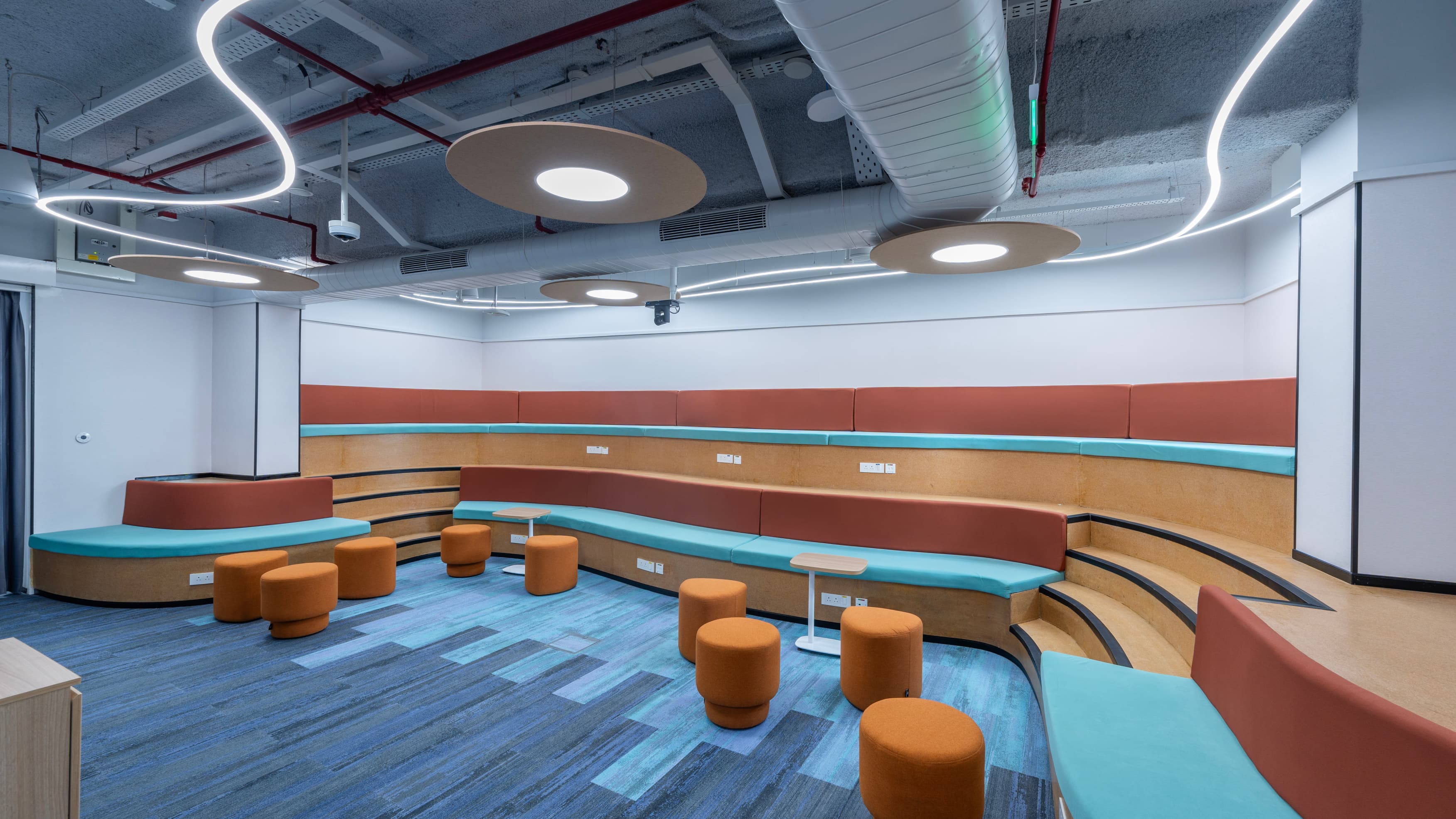 Amphitheatres on the work floors host town halls and team stand-ups. Exposed ceilings are treated with acoustic spray and circular baffles to temper background noise in an open plan.