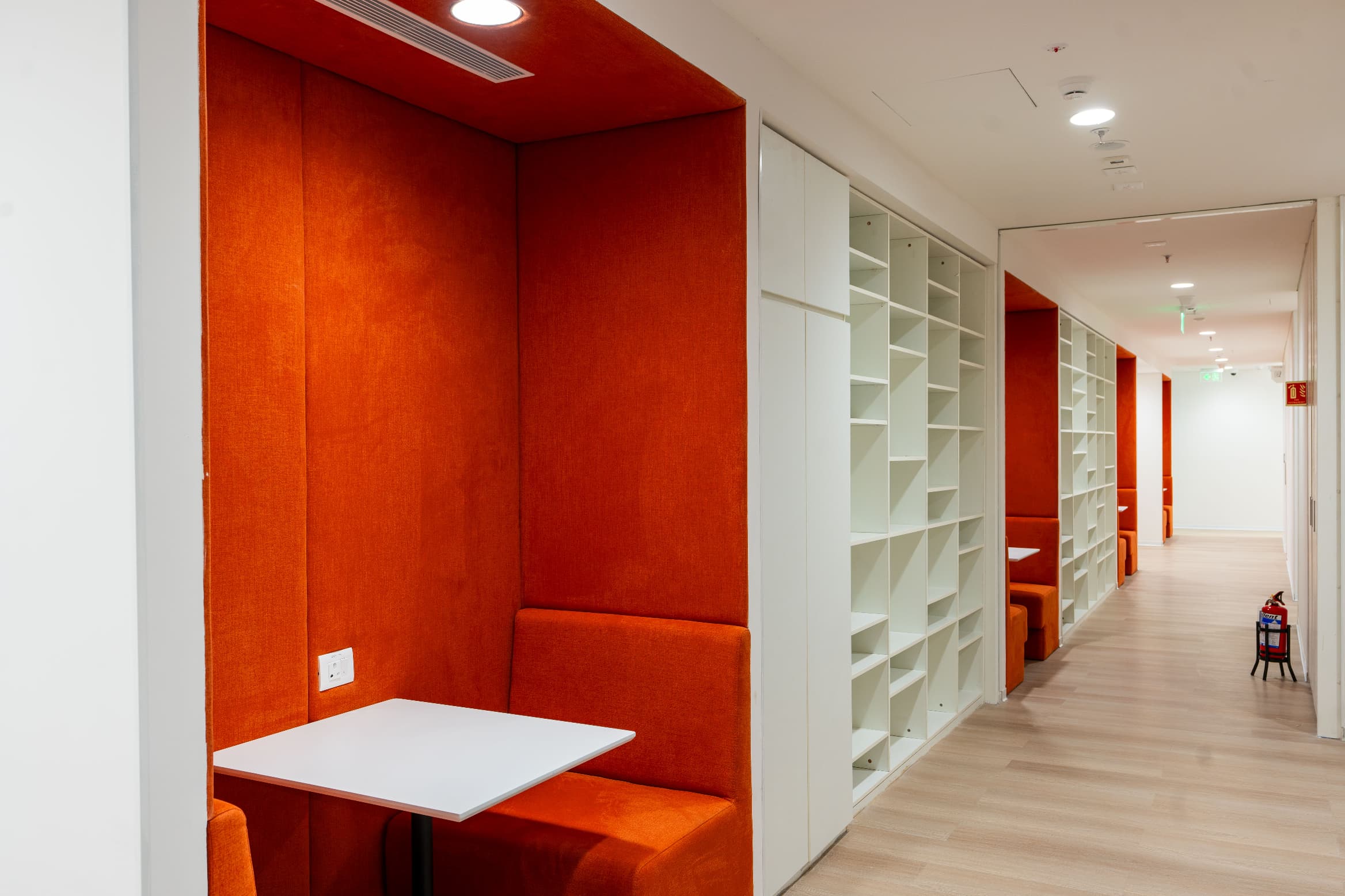 The spine between the two zones is conceived as a library corridor, lining the route with upholstered booths, open shelving and hydration points.