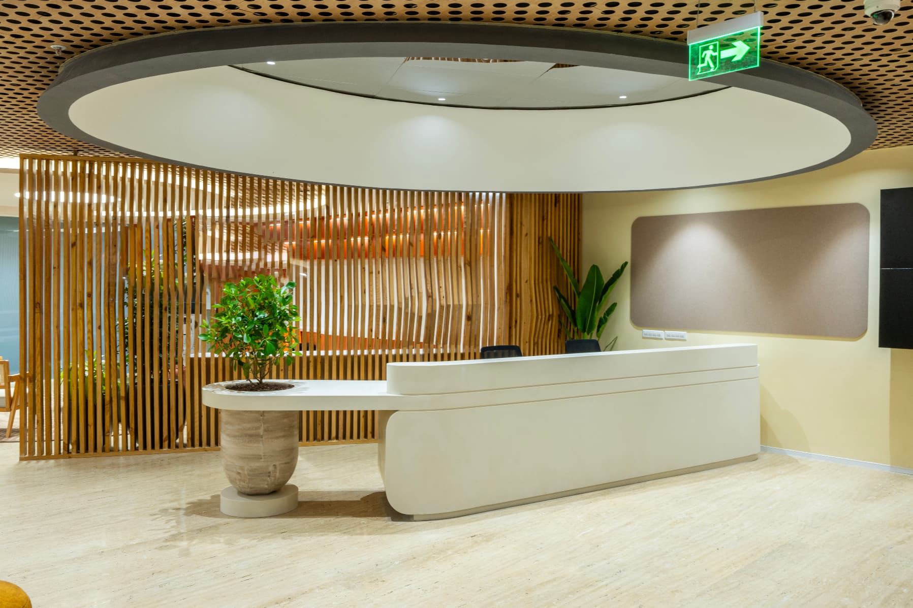 Baffle walls of slender 50mm wooden fins screen the arrival space, adding lightness and rhythm. Overhead, perforated timber panels and curved gypsum forms carry a gentle sense of movement into the main circulation spine.