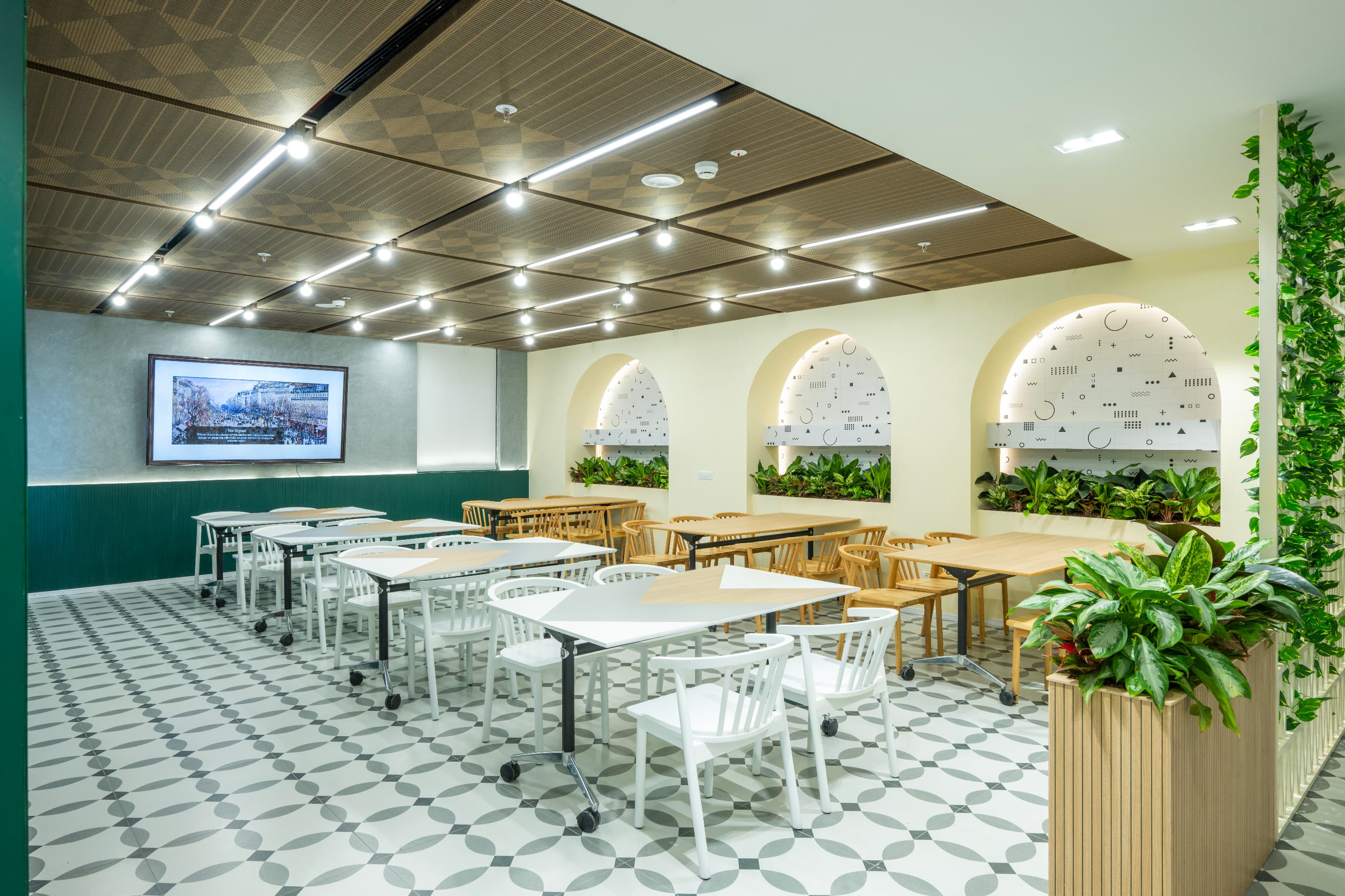 Arched niches planted with greenery line the cafeteria beneath a timber checkerboard ceiling. Warm South Indian ochres, terracottas and deep greens ground the restrained foundation in regional warmth.