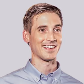 Smiling middle-aged man with blue eyes and short hair wearing a purple collared shirt.