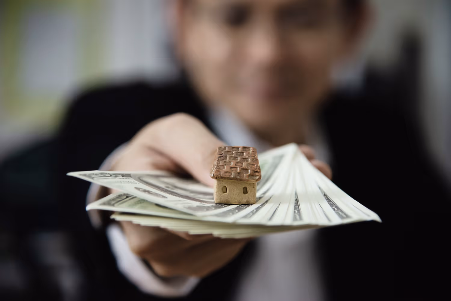 A person holding a small house on top of a stack of moneyAI-generated content may be incorrect.