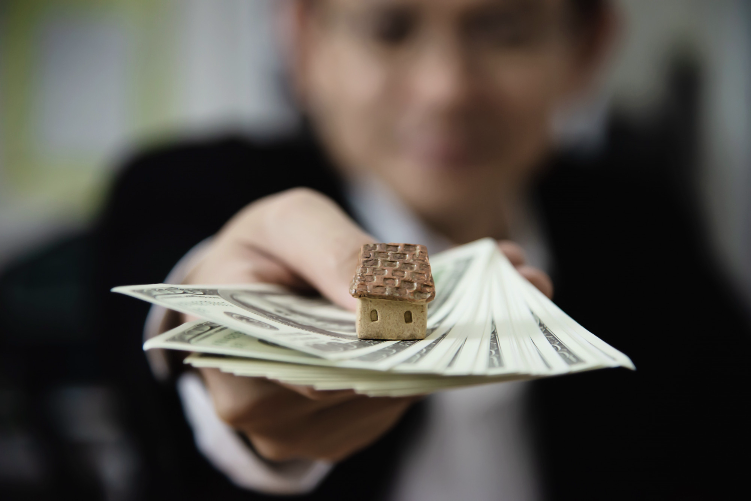 A person holding a small house on top of a stack of moneyAI-generated content may be incorrect.