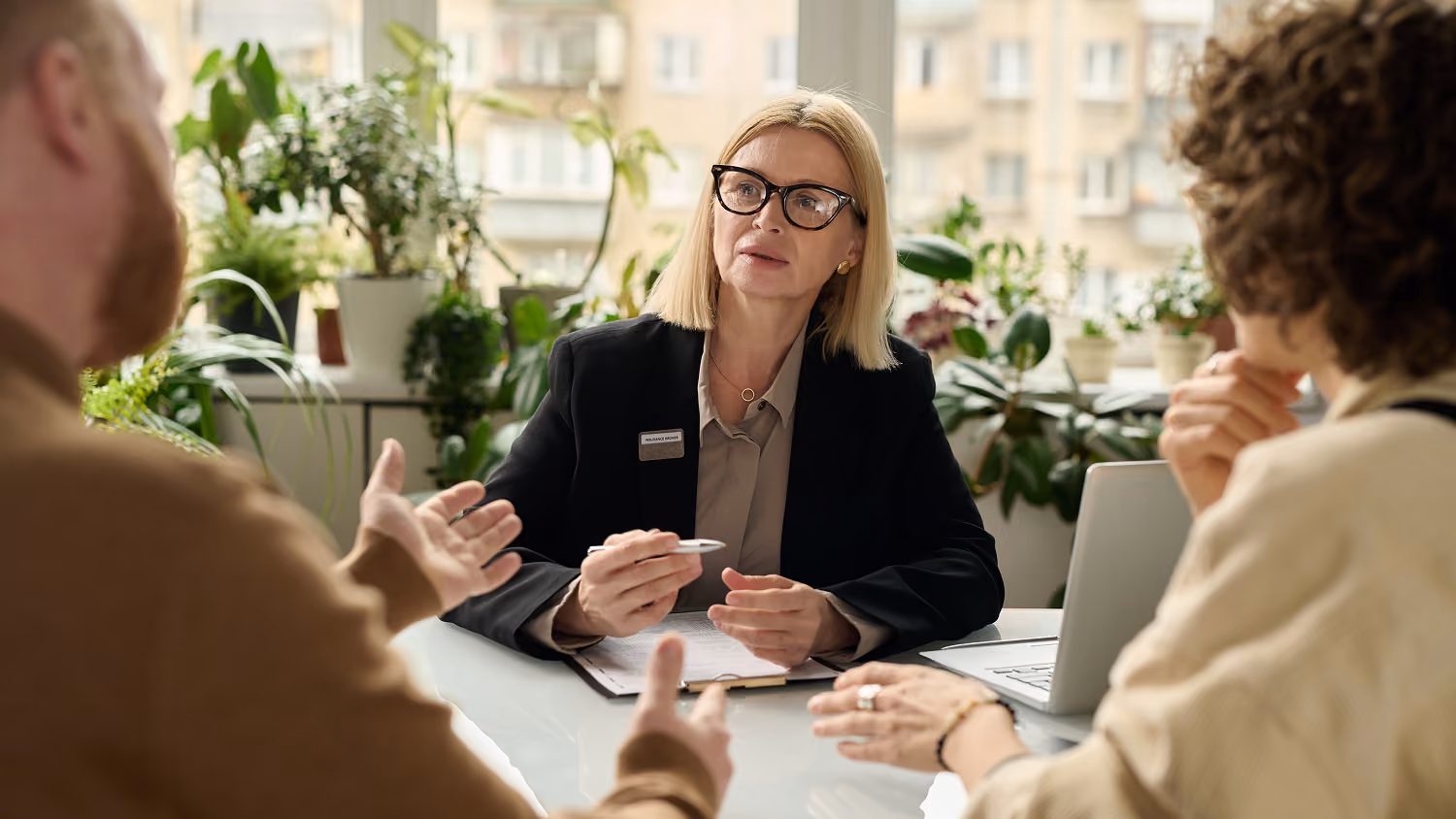 Female employee in glasses consulting a couple at a desk with plants in the background.