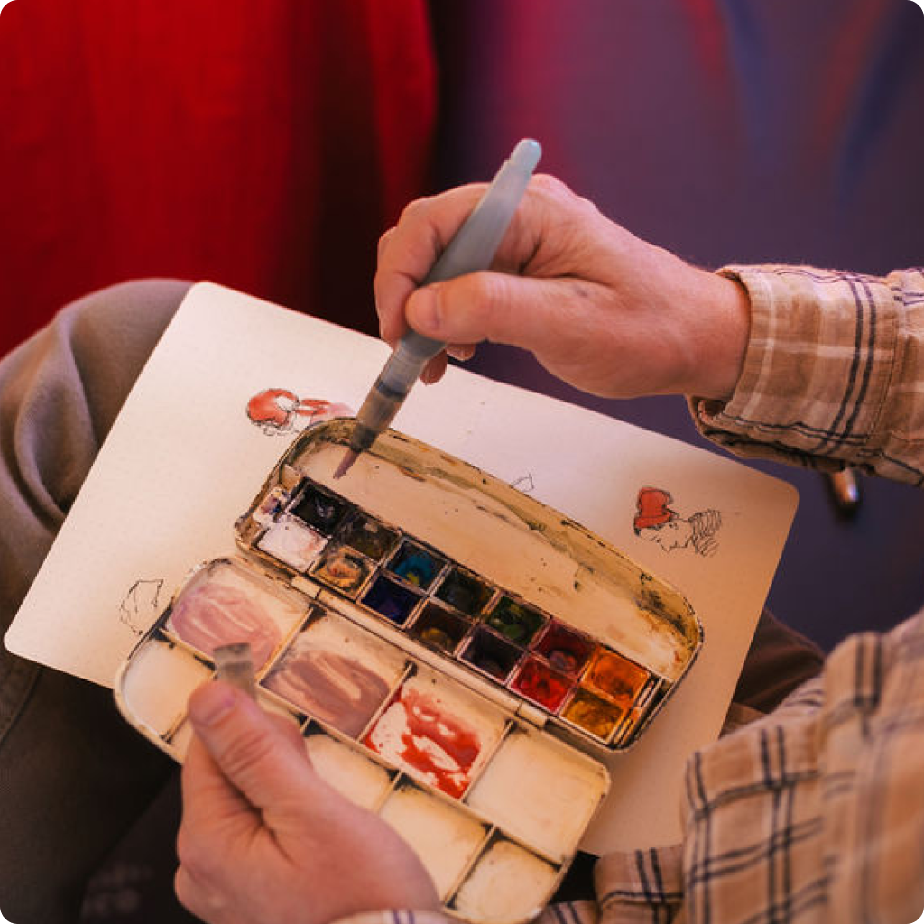 Artist mixing watercolor paints while working on a sketch in a notebook.
