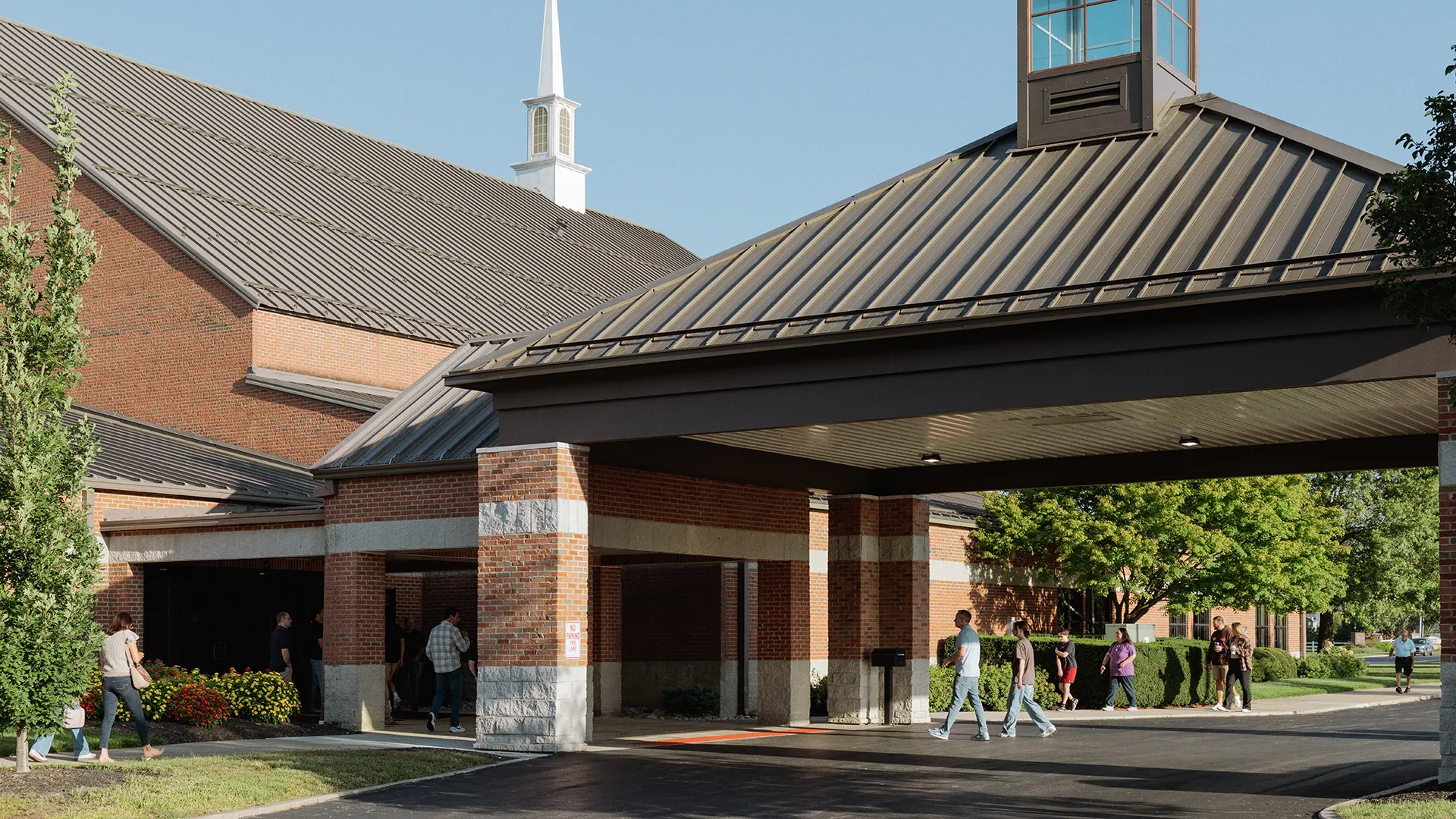 Families and young adults arriving at Northwest Bible Church on a Sunday morning, greeted by a sign reading "We're so glad you're here!"