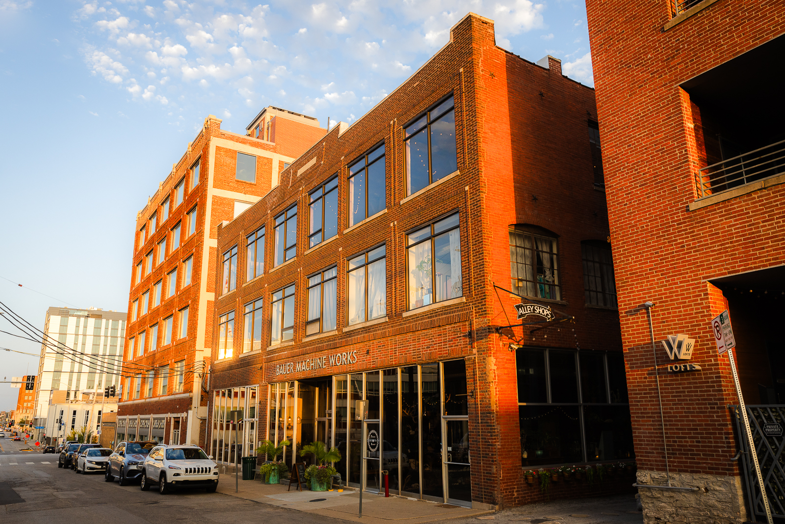 Brick building named Bauer Machine Works with cars parked along the street at sunset.