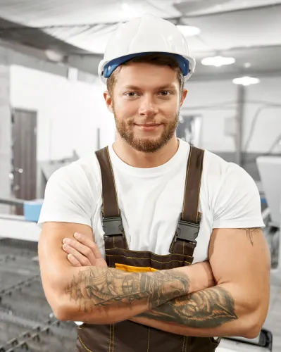 Construction worker in hard hat smiling with crossed arms in workshop