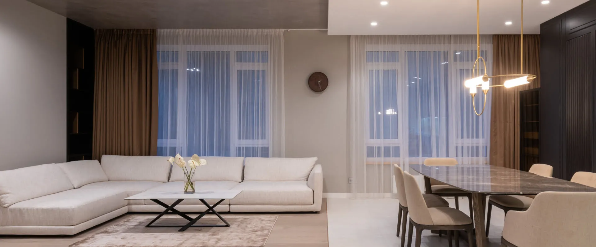 Modern living room with white sofa, dining area, and sheer curtained windows