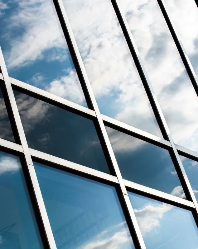 Modern glass windows reflecting cloudy sky with geometric white frames