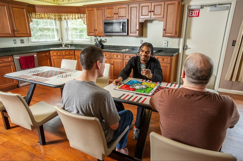 Adult foster care residents engaged in a colorful board game at a communal kitchen table, showcasing indoor winter wellness activities for maintaining engagement and social interaction.