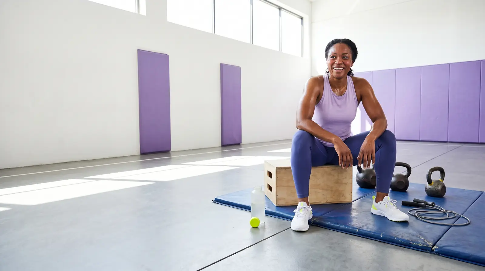 Woman resting on a plyo box beside kettlebells after a workout — GobyMeds sermorelin for women