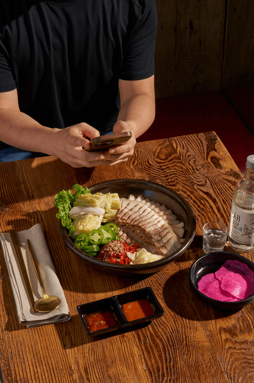 A customer taking a photo of Bossam at Hangari Kalguksu (항아리 칼국수) – Bossam (보쌈) platter beautifully presented with traditional sides, served in Koreatown, Los Angeles