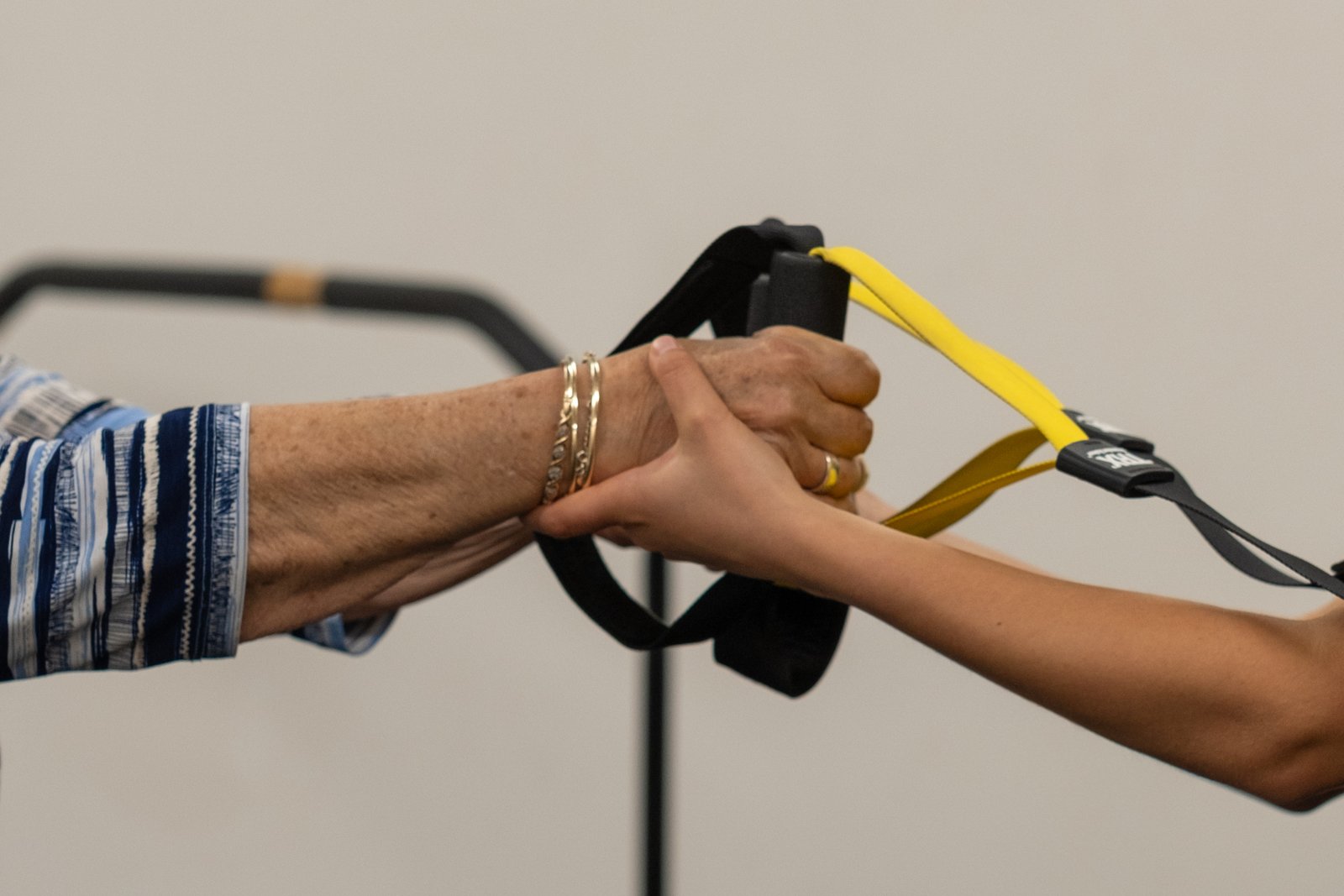 A clinician's hand supporting a client's hand on a TRX handle at The Biomechanics