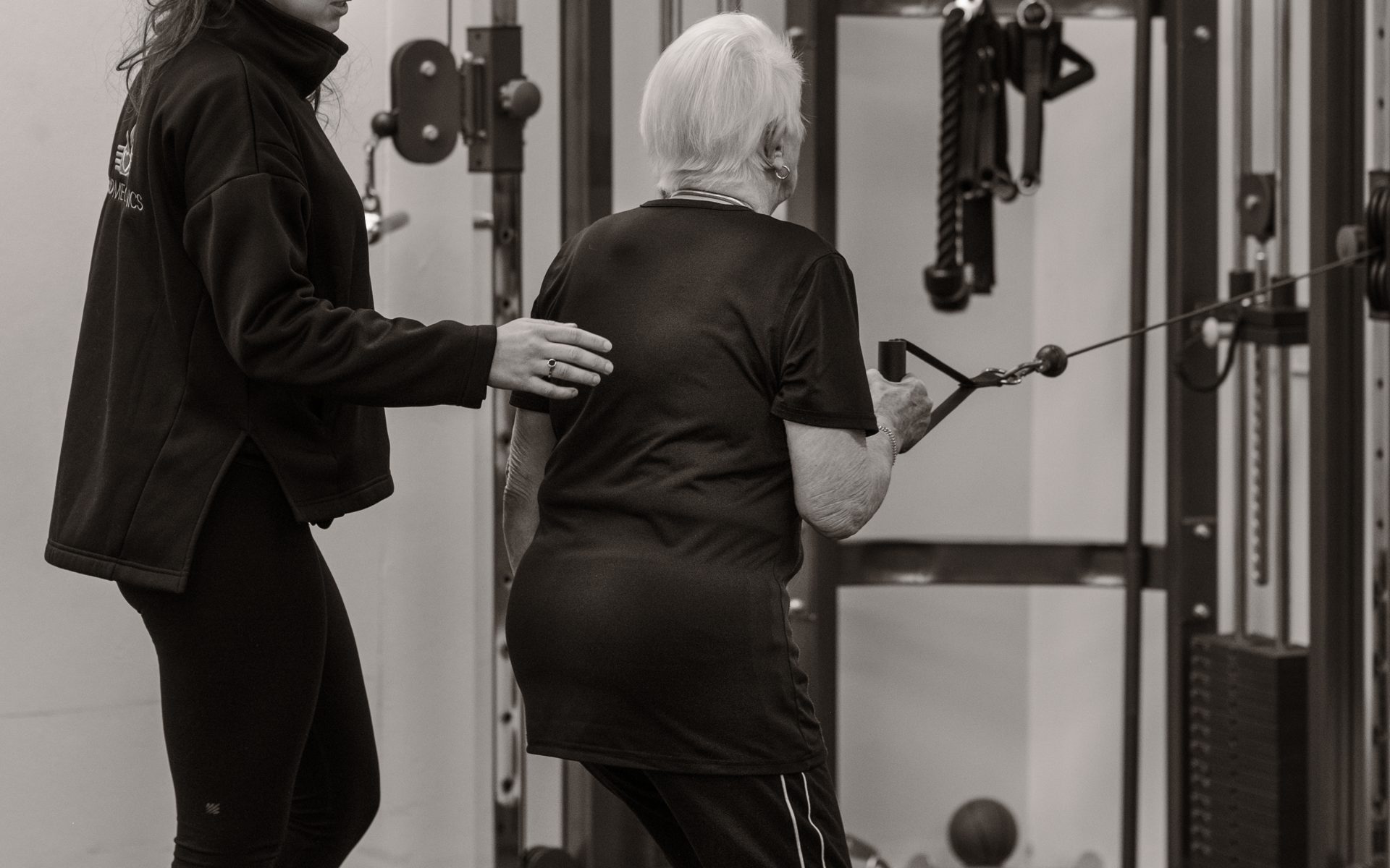 An exercise physiologist supporting an older woman through a cable exercise at The Biomechanics