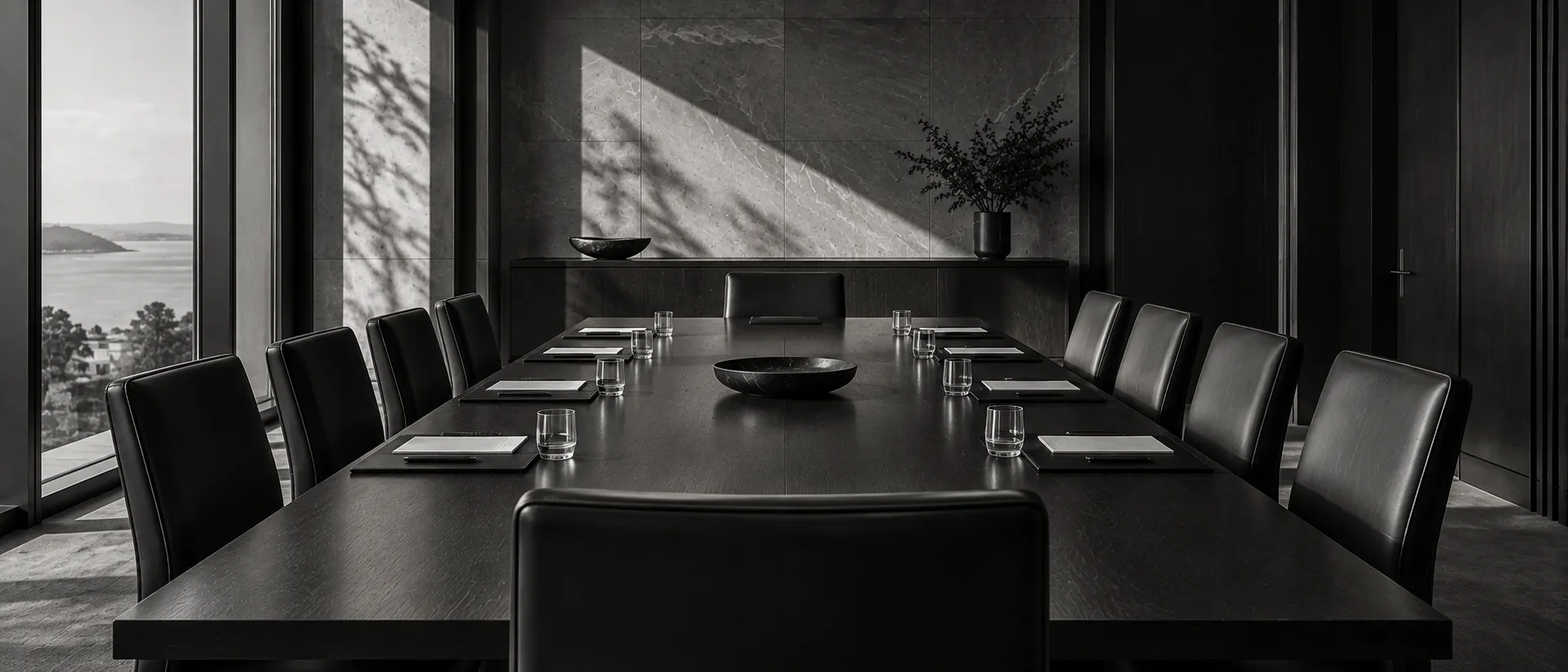An empty, formally set governance meeting table, in monochrome.