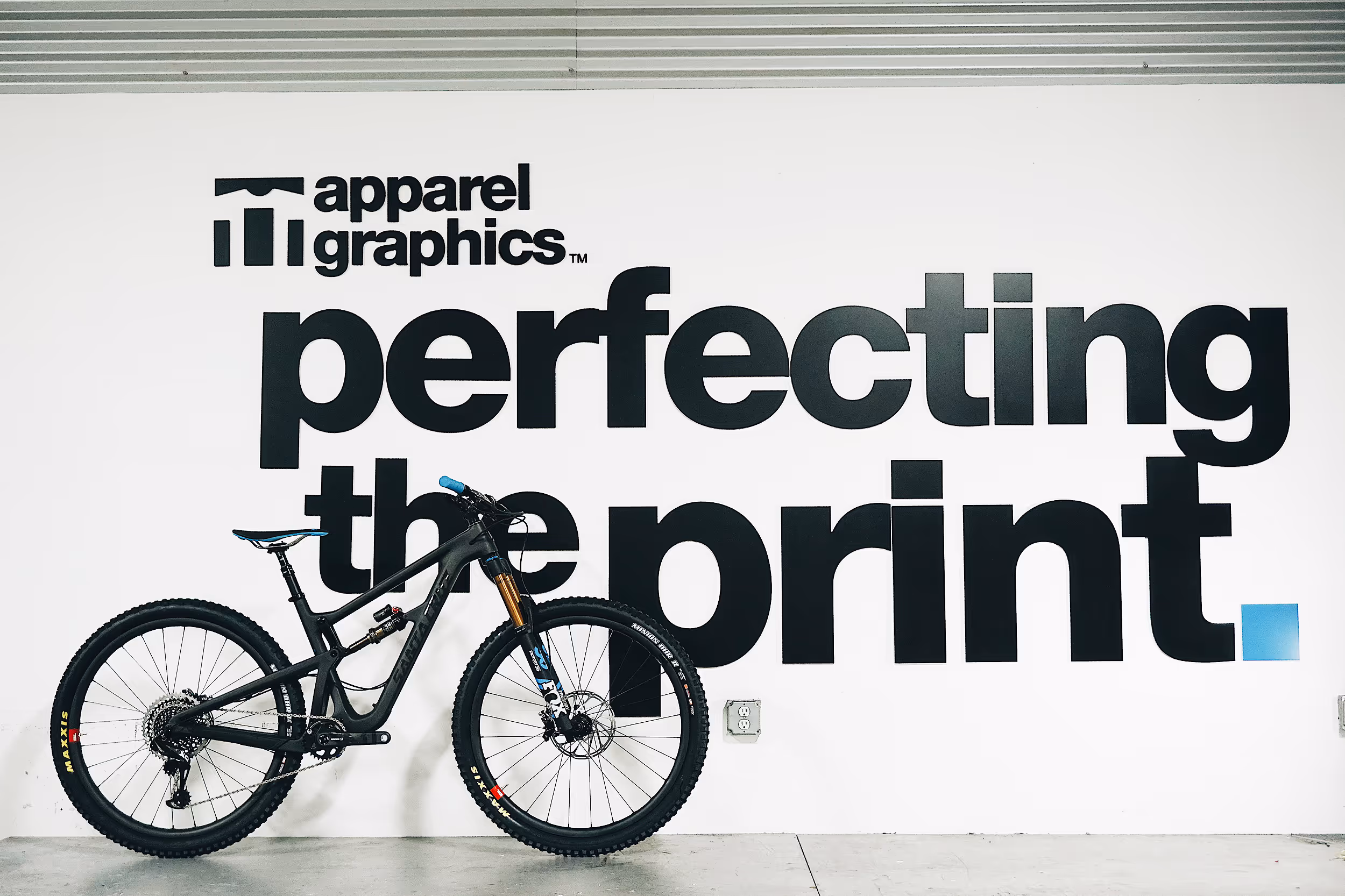 An image featuring a Santa Cruz Bike in front of an Apparel Graphics sign.