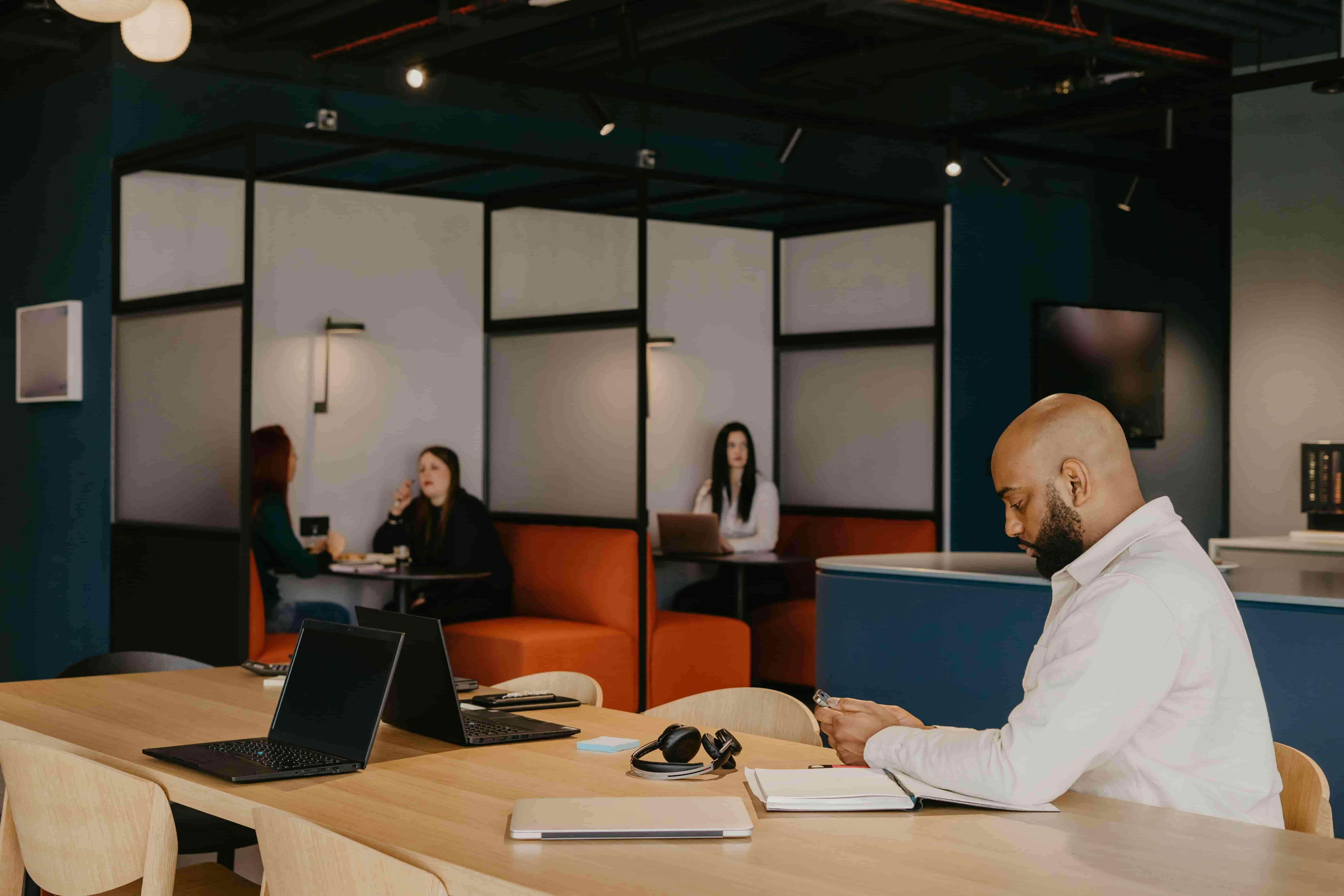 Coworking space with people working at shared tables and booth seating in a modern, softly lit office.