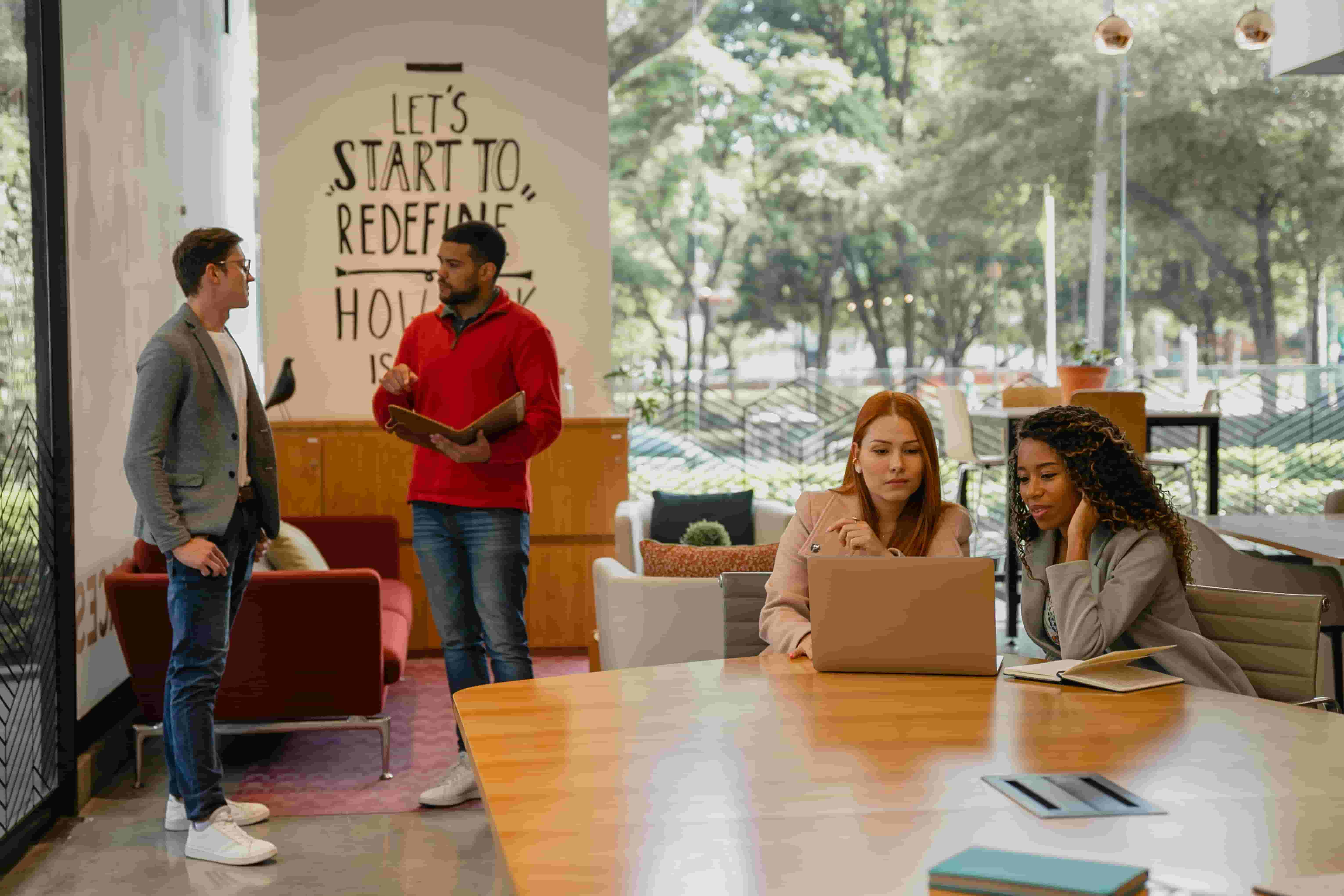 People collaborating in a bright coworking lounge with large windows, modern seating, and shared workspaces.”