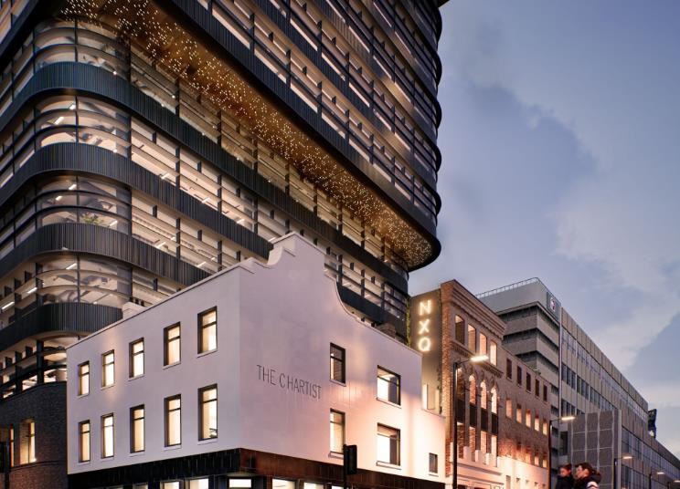 Modern high-rise office development rising above the restored historic ‘The Chartist’ building, with illuminated upper floors and surrounding city architecture at dusk.