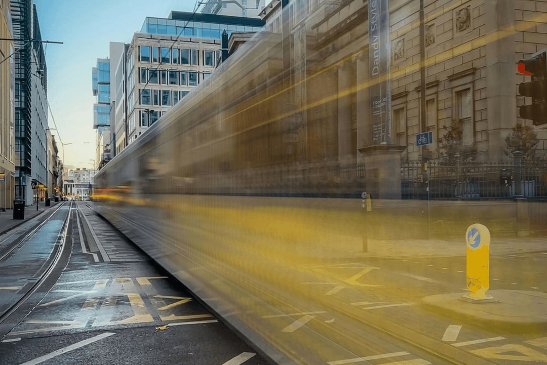 Blurred Manchester tram moving through the city centre between modern and historic buildings.
