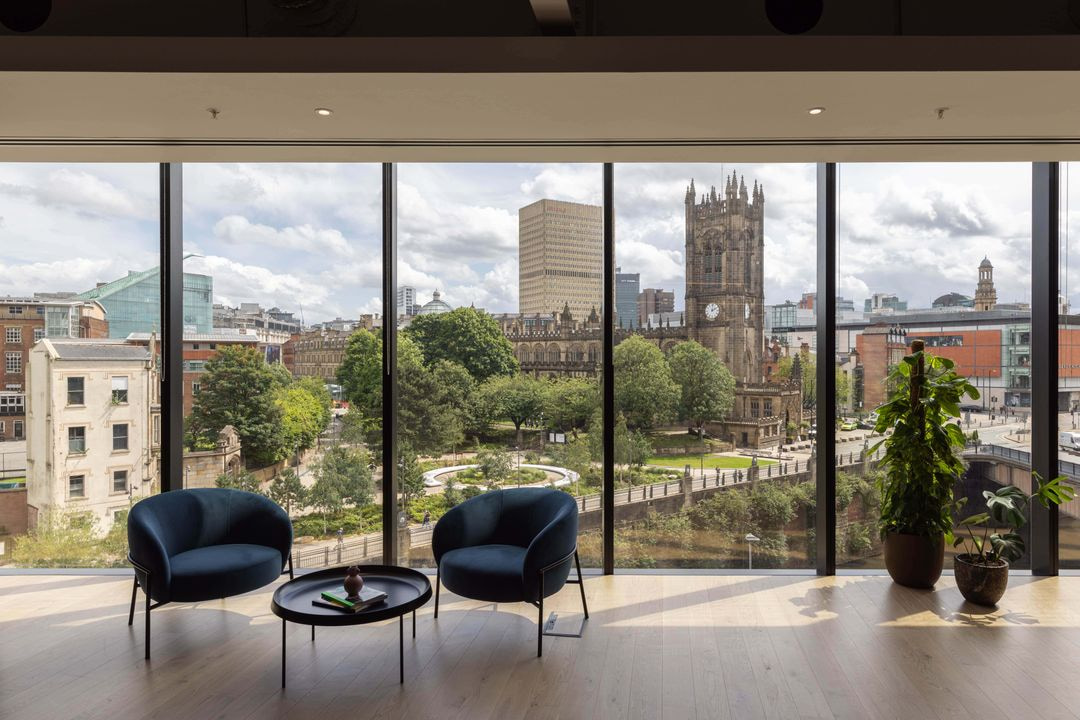Modern office lounge with panoramic floor-to-ceiling windows overlooking Manchester Cathedral and the city skyline.