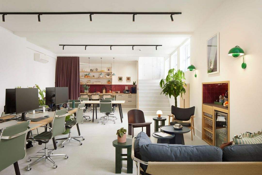 Stylish open-plan coworking office with modern desks, a lounge area, indoor plants, and a bright communal kitchen.