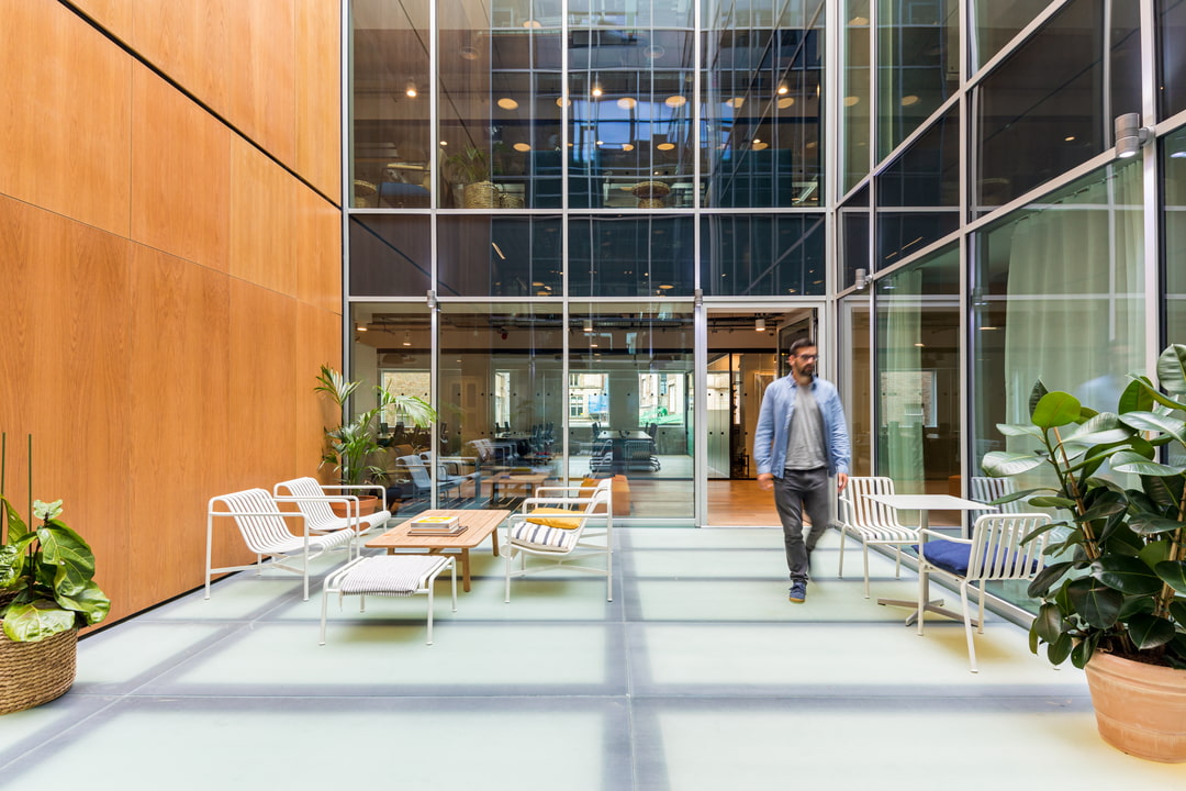 Bright serviced office atrium with contemporary lounge furniture, glass partitions, greenery, and open breakout space.
