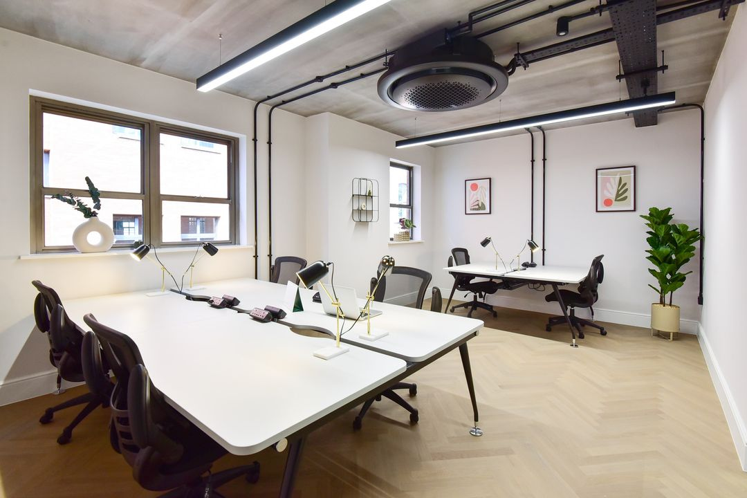 Bright contemporary private office with white desks, ergonomic chairs, industrial-style ceiling, large windows, modern desk lamps and indoor plants.