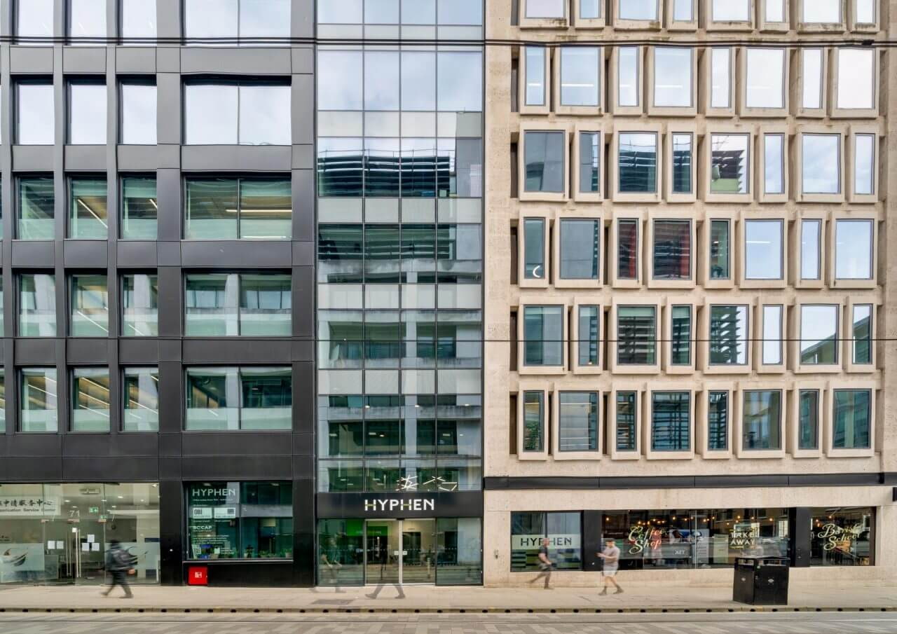 Street-level view of the Hyphen office building with modern glass façade and geometric window design in an urban city centre.