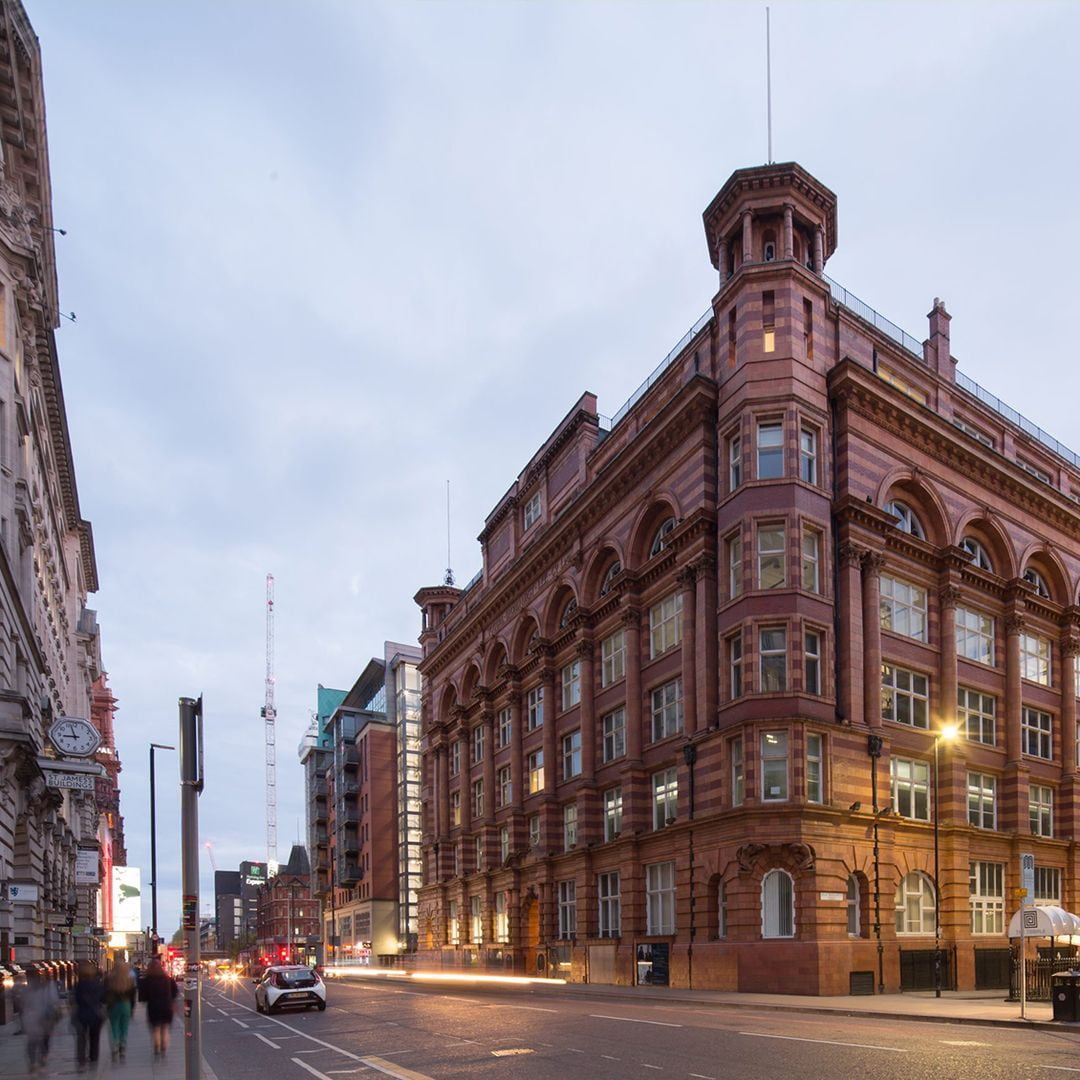 Historic red-brick office building on a busy city street at dusk, featuring arched windows and classic architecture.