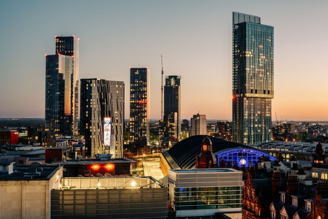 Manchester city skyline at sunset with modern skyscrapers and the illuminated Manchester Central building.