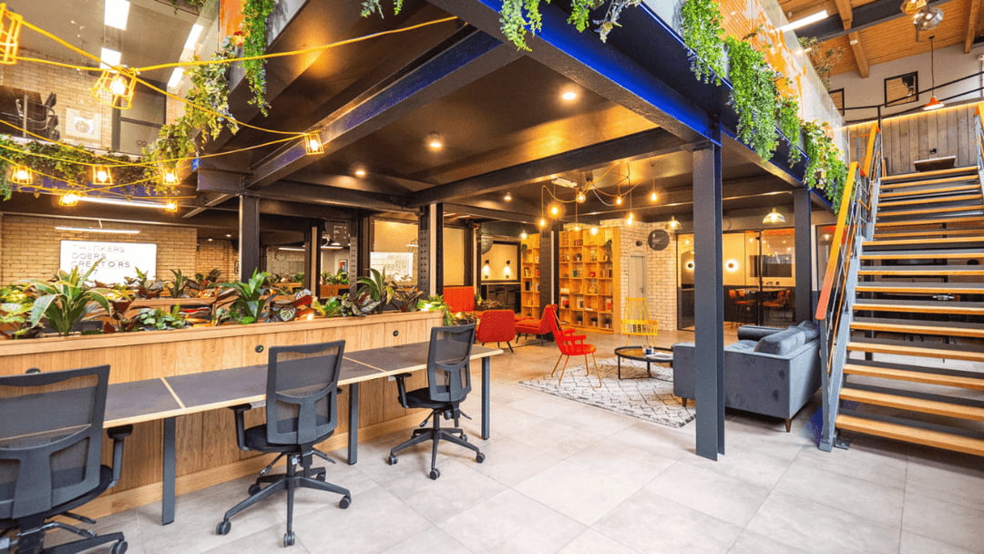 “Modern coworking space with shared desks, greenery, lounge seating and an industrial mezzanine design.