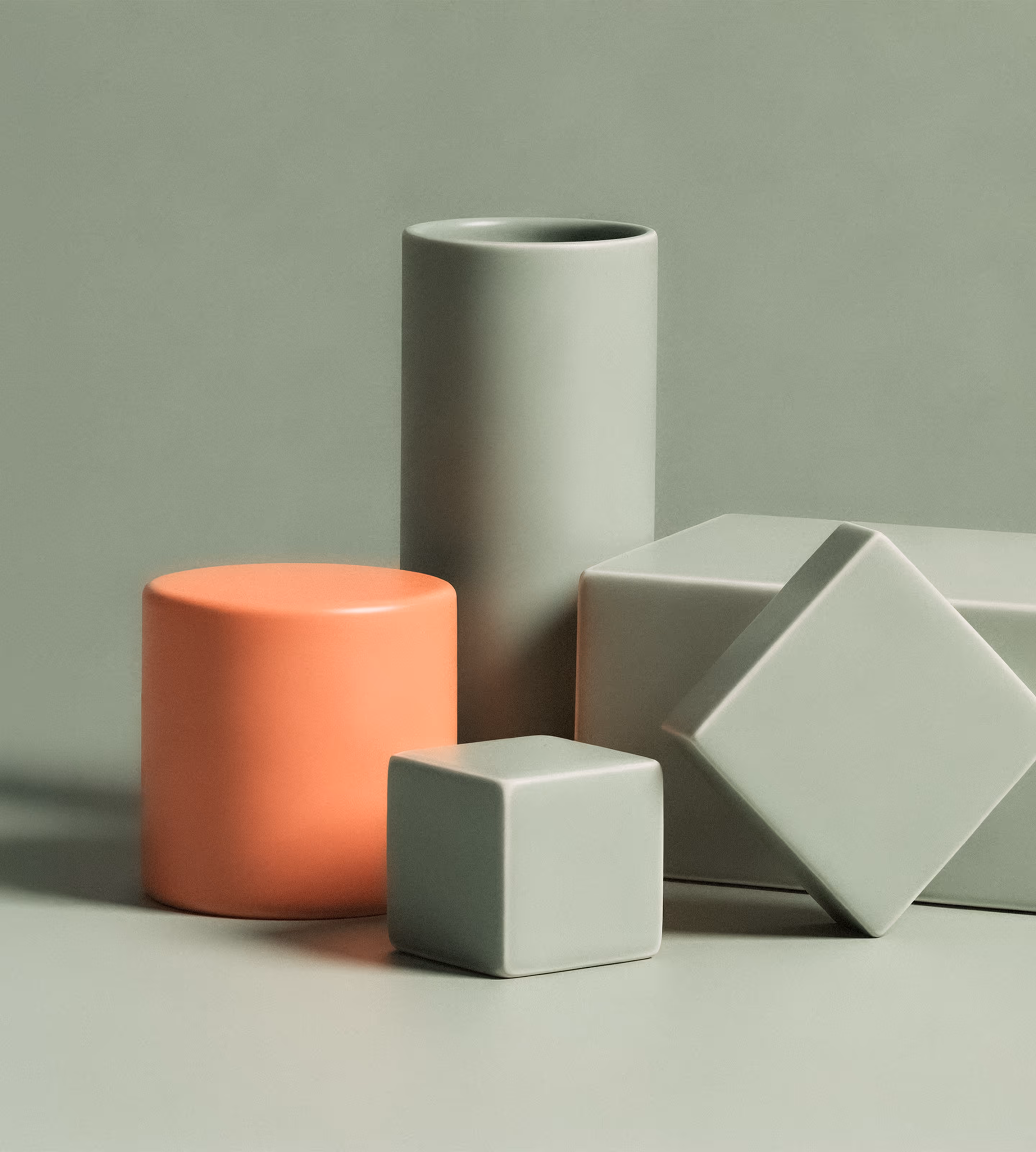 Formes géométriques en céramique mate vert sauge et orange, cylindres et cubes disposés ensemble.